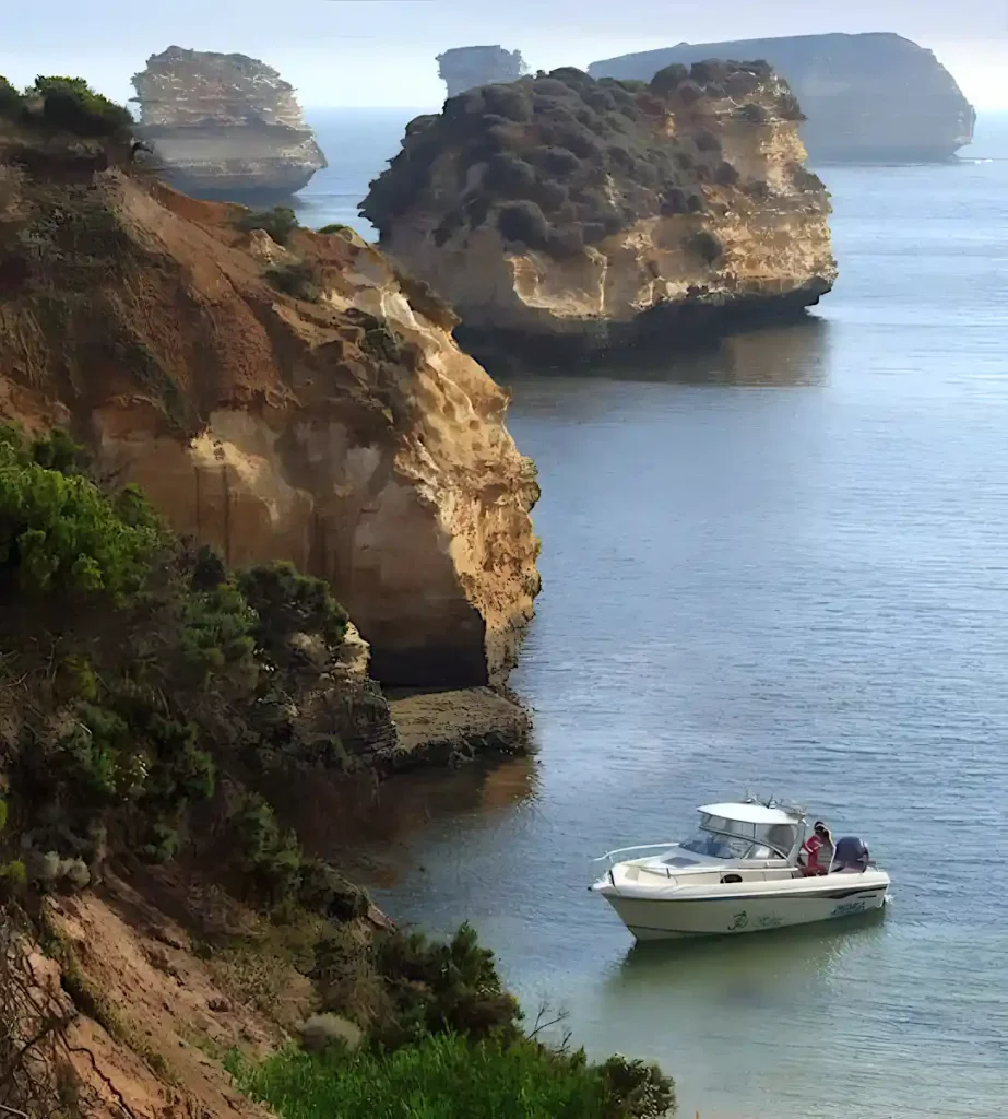 A small boat with people on board is anchored near the shore in the Bay of Islands, surrounded by calm sea and rugged cliffs.