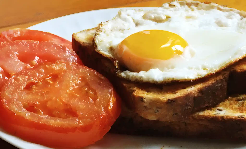 Closeup of two slices of grilled tomato and a fried egg on two slices of wholegrain toast, all on a white plate.