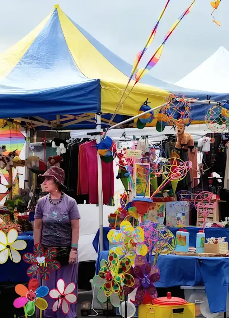 A woman wanders among colorful market wares and a large tent at the Port Fairy Folk Festival